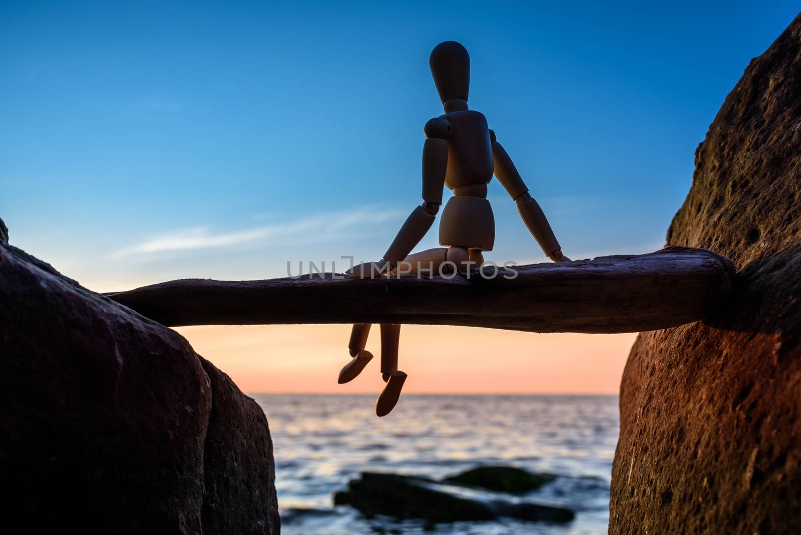 Wooden mannequin sitting on a stick between boulders