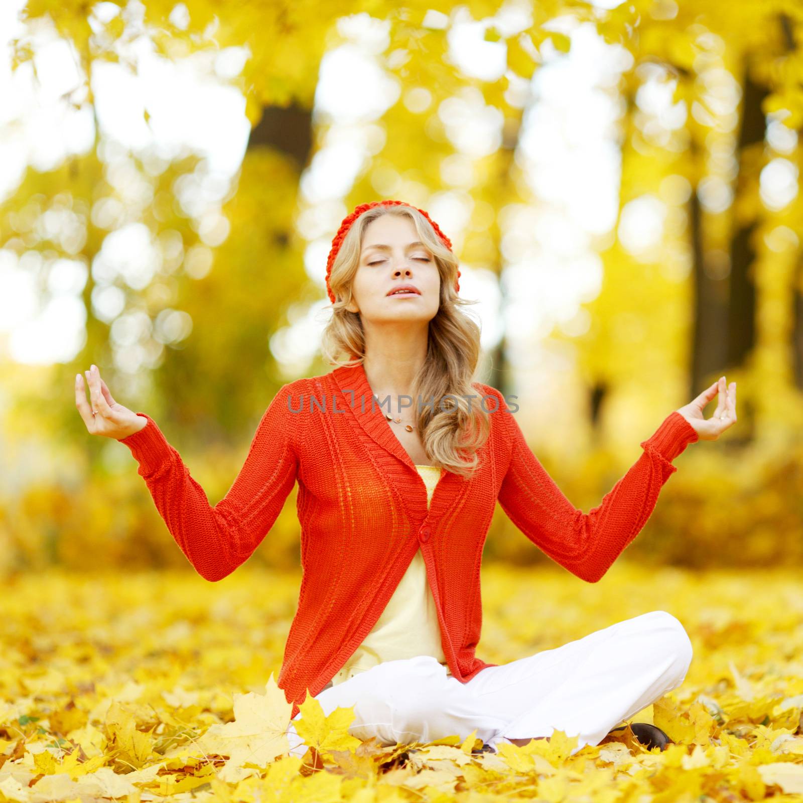 Beautiful young woman sitting in autumn park in lotus yoga position