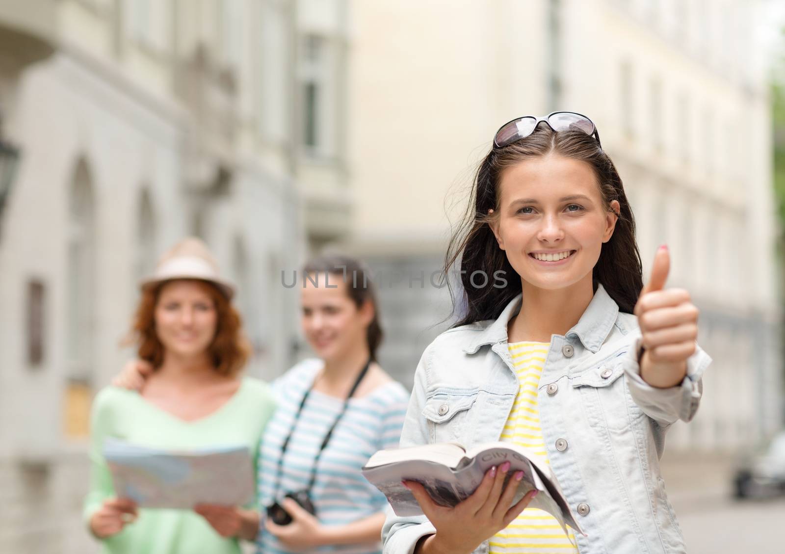 tourism, travel, holidays and friendship concept - smiling teenage girls with city guide, map and camera showing thumbs up outdoors