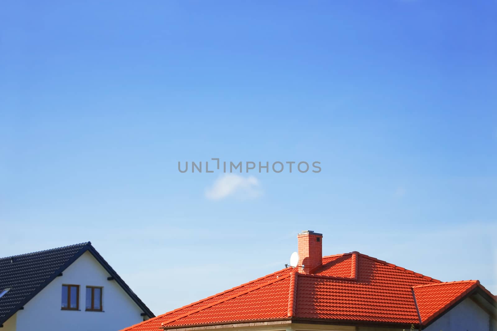 Red roof of new detached houses against blue sky.