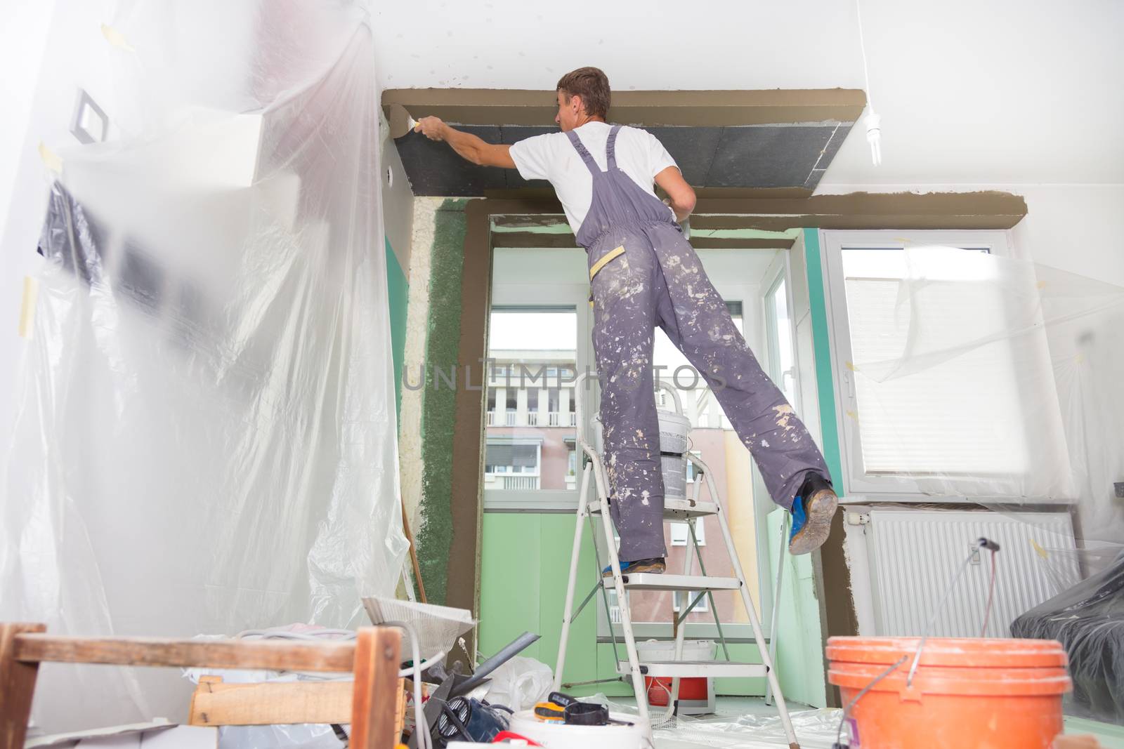 Thirty years old manual worker with wall plastering tools inside a house. Plasterer renovating indoor walls and ceilings with float and plaster.