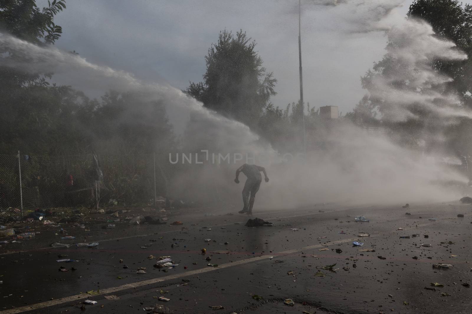 SERBIA, Horgos: A man ducks as Hungarian police fire tear gas and water cannons into the refugees in the Serbian border town of Horgos on September 16, 2015, after Hungary closed its border in an effort to stem the wave of refugees entering the country. 