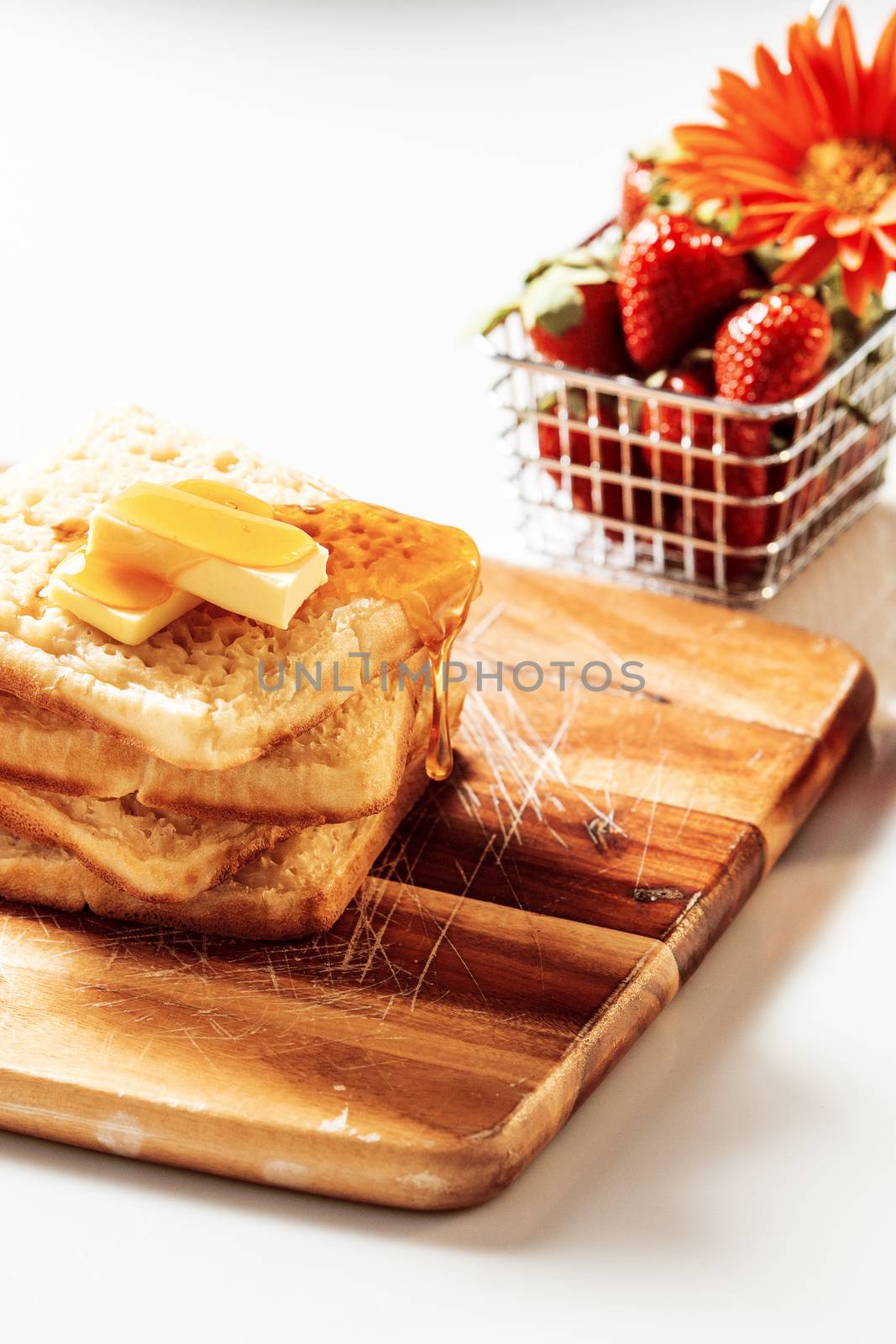 Toasted crumpets with honey drizzled over them and strawberries in the background.