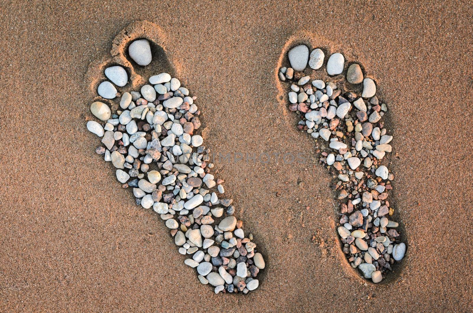 Bare feet made of pebble on the sandy beach