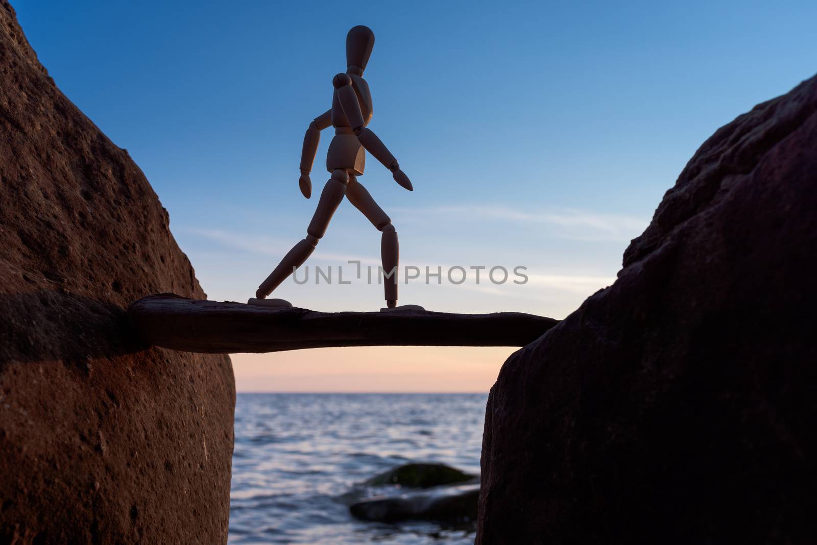 Wooden mannequin walking on a stick between boulders