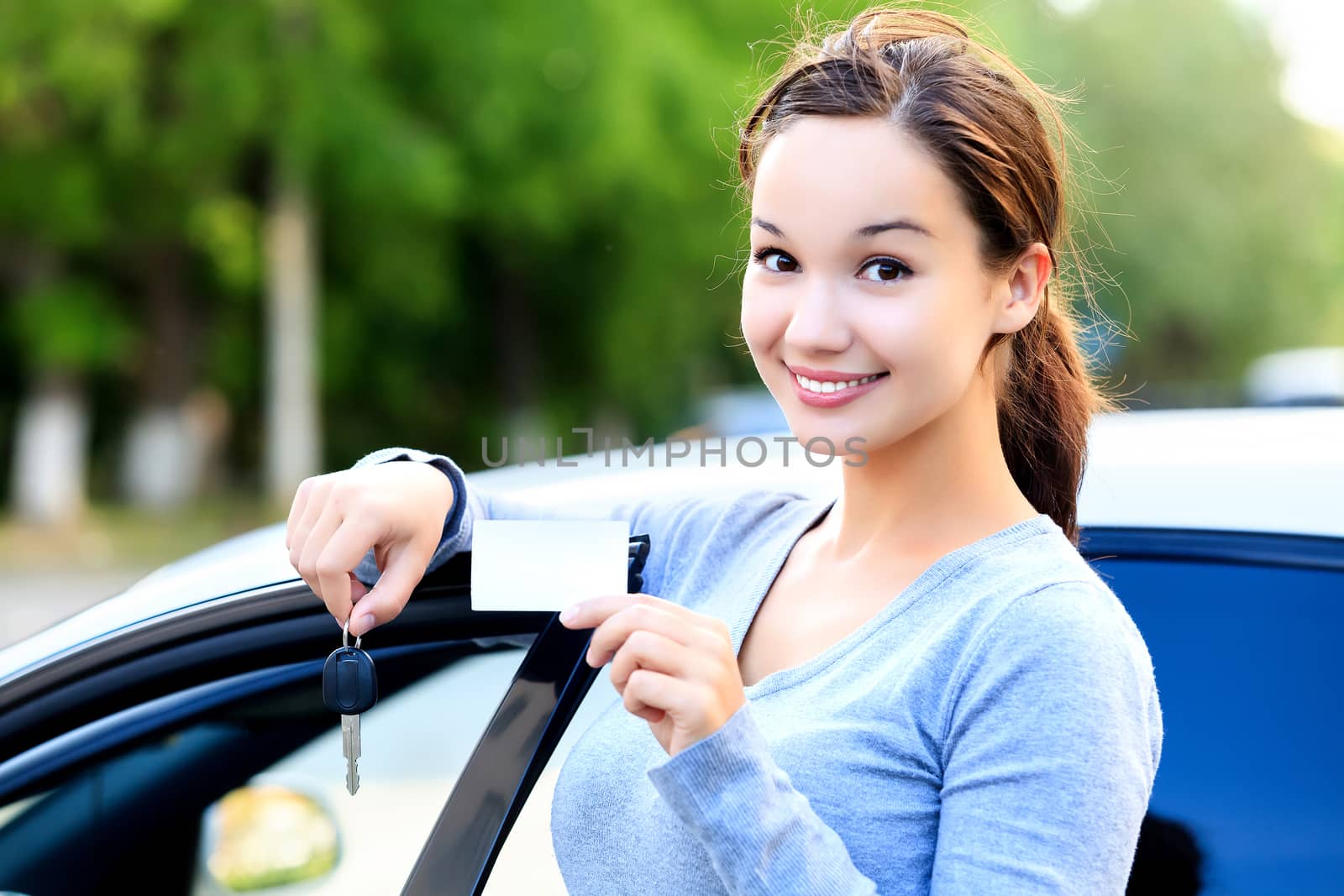 Woman stands beside a car and shows keys and white card by Nobilior