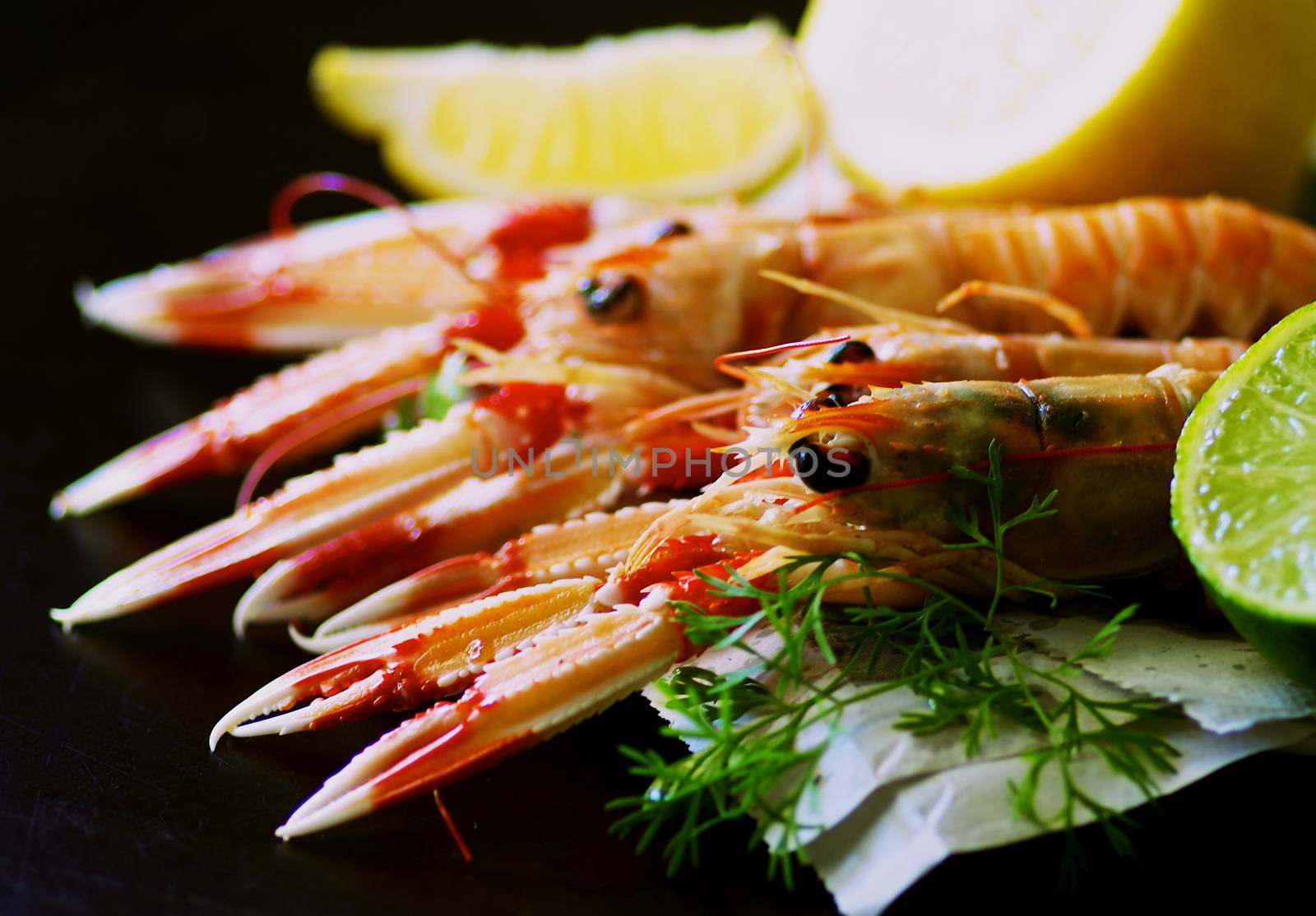 Delicious Grilled Langoustines  on Newspaper with Lime and Lemon closeup on Dark Wooden background. Focus on Animal Eyes on Foreground