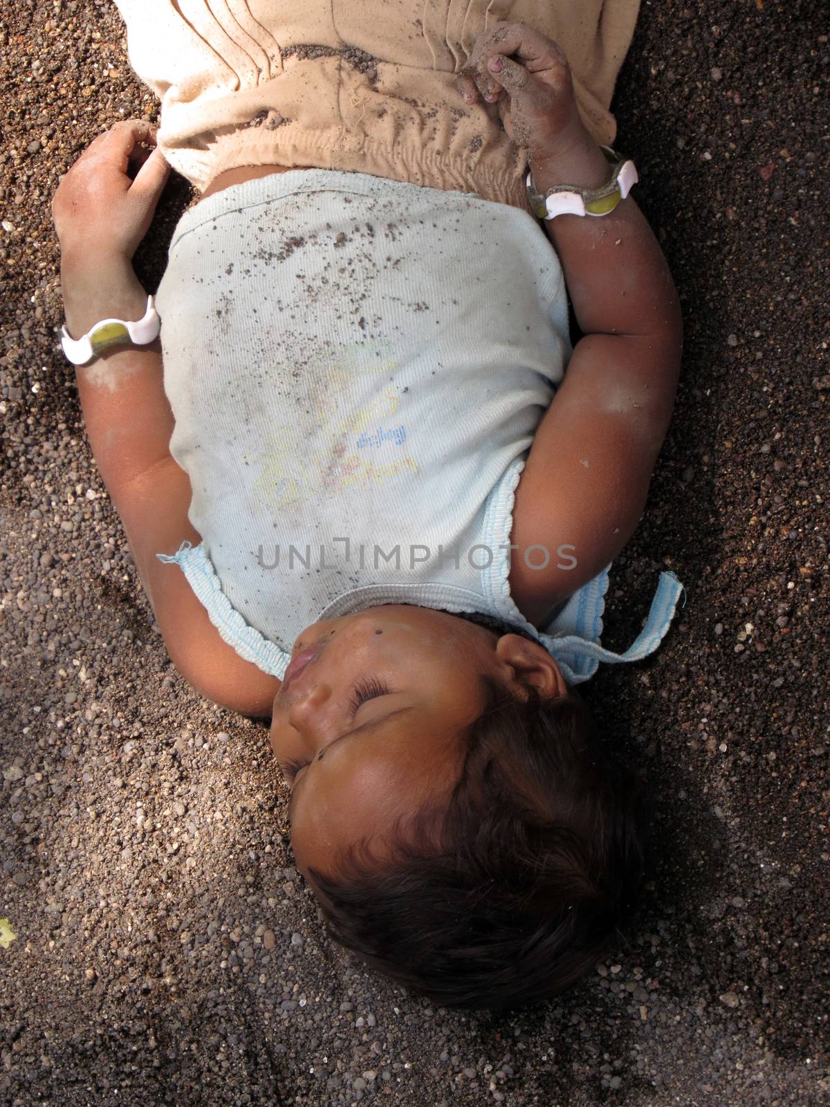 A poor little child sleeping under the sun and shade in the soil used for construction.                               