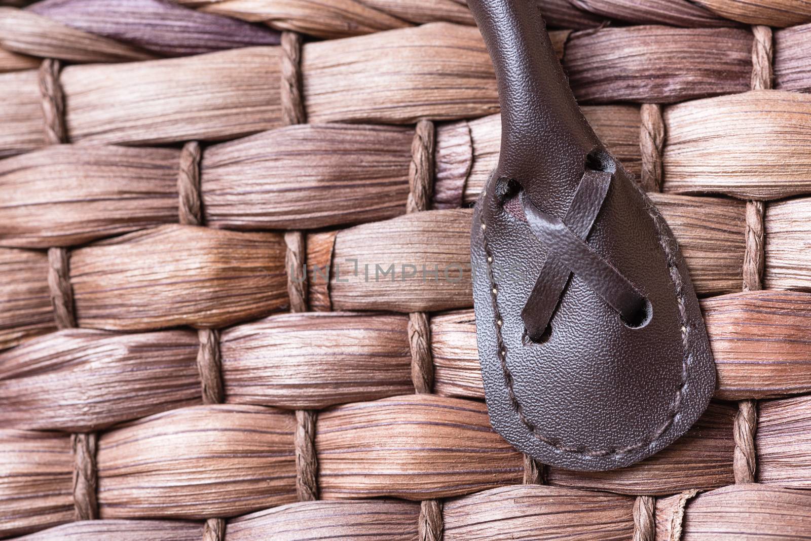 A macro shot of a leather handle stitched into a brown wovel wicker basket.