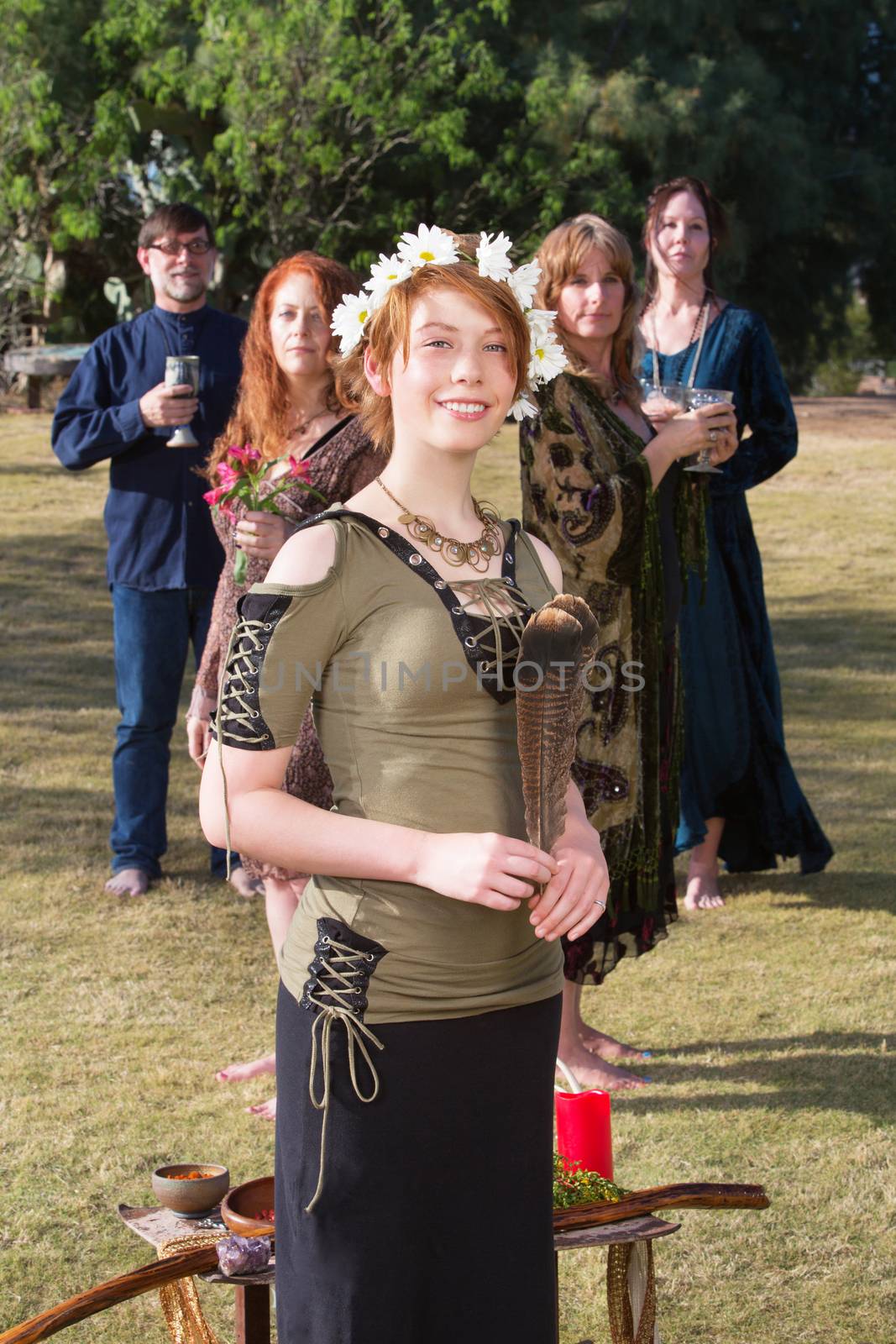 Cute Caucasian young witch holding feather near altar outdoors