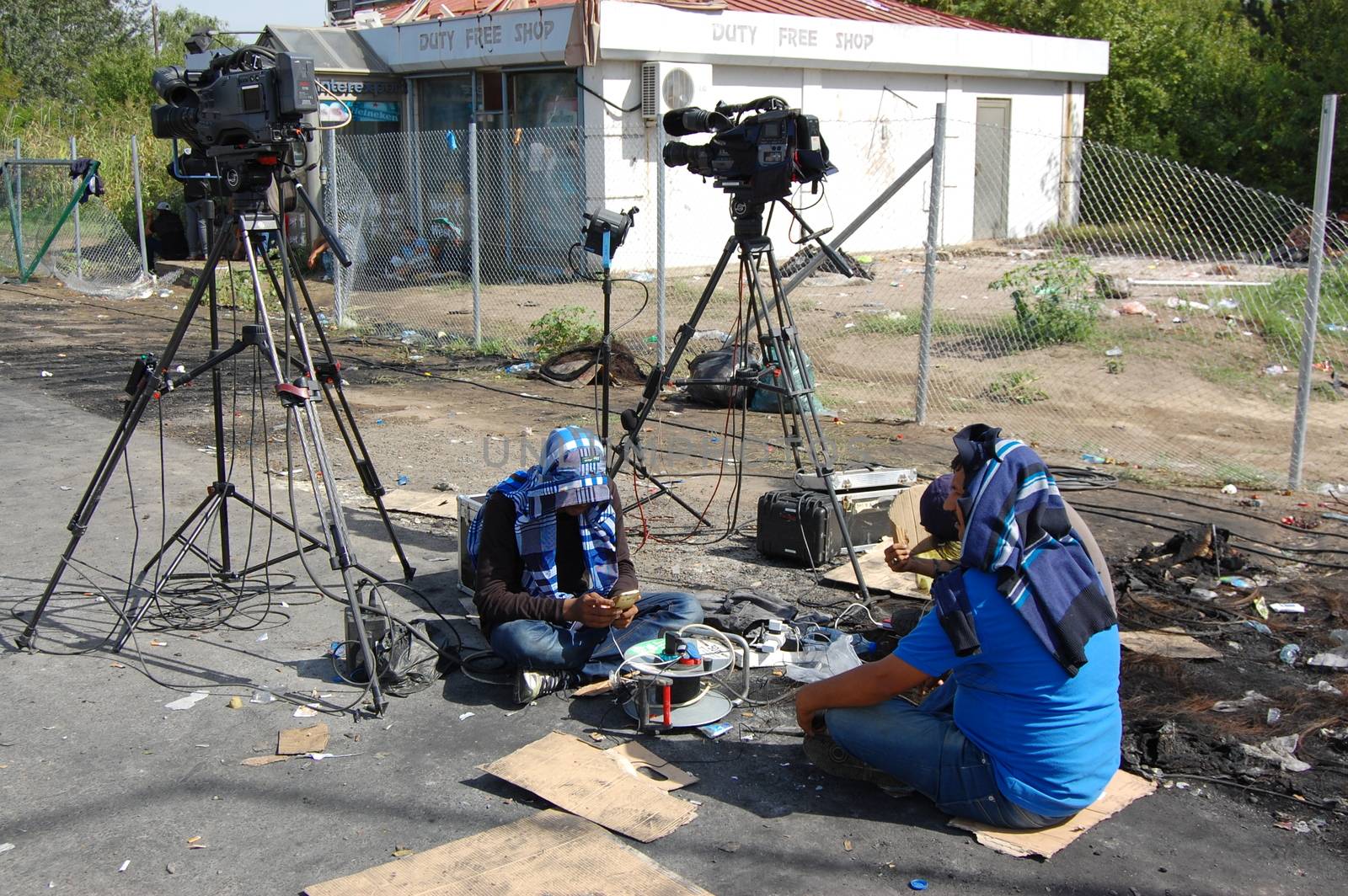 SERBIA, Horgo�: Two men sit near cameras at the Serbia-Hungary border in Horgo�, Serbia on September 17, 2015. Recently the migrants have clashed with police forcing the police to use tear gas and water cannons to hold the refugees at bay. The migrants demanded that the razor-wire fence be opened, which would allow them to continue their journey though Europe. 