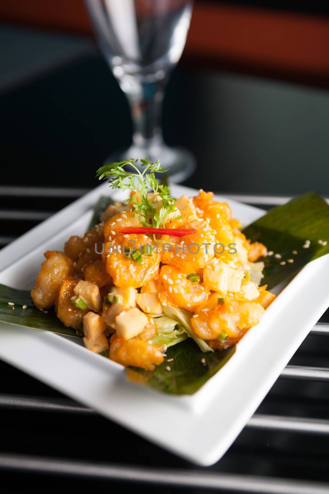 Thai crispy shrimp dish with apple and sesame seeds presented beautifully on a white square plate with chopsticks.