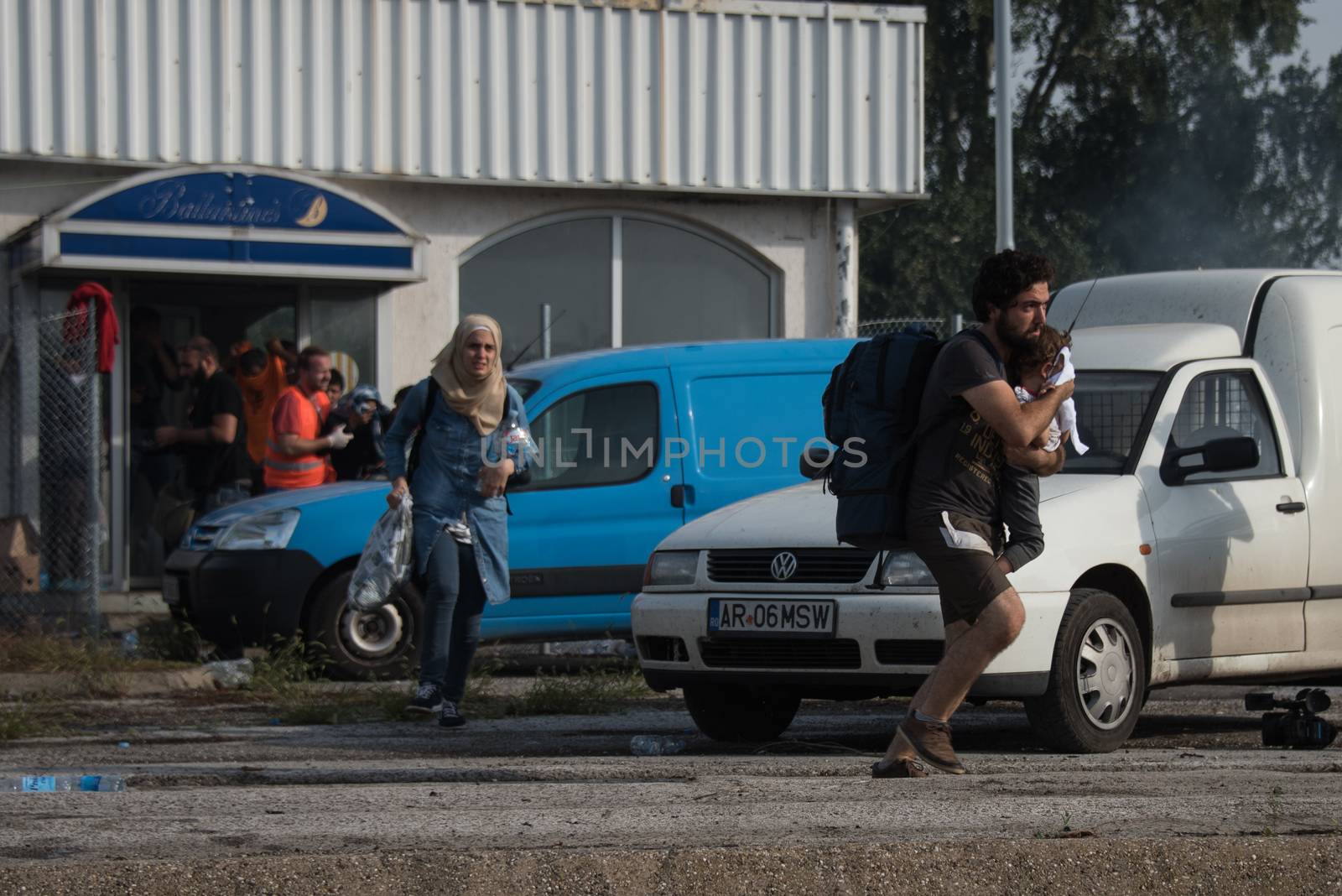 SERBIA, Horgos: A man runs with a small child as Hungarian riot police clash with refugees waiting to cross the border from the Serbian border town of Horgos on September 16, 2015. 