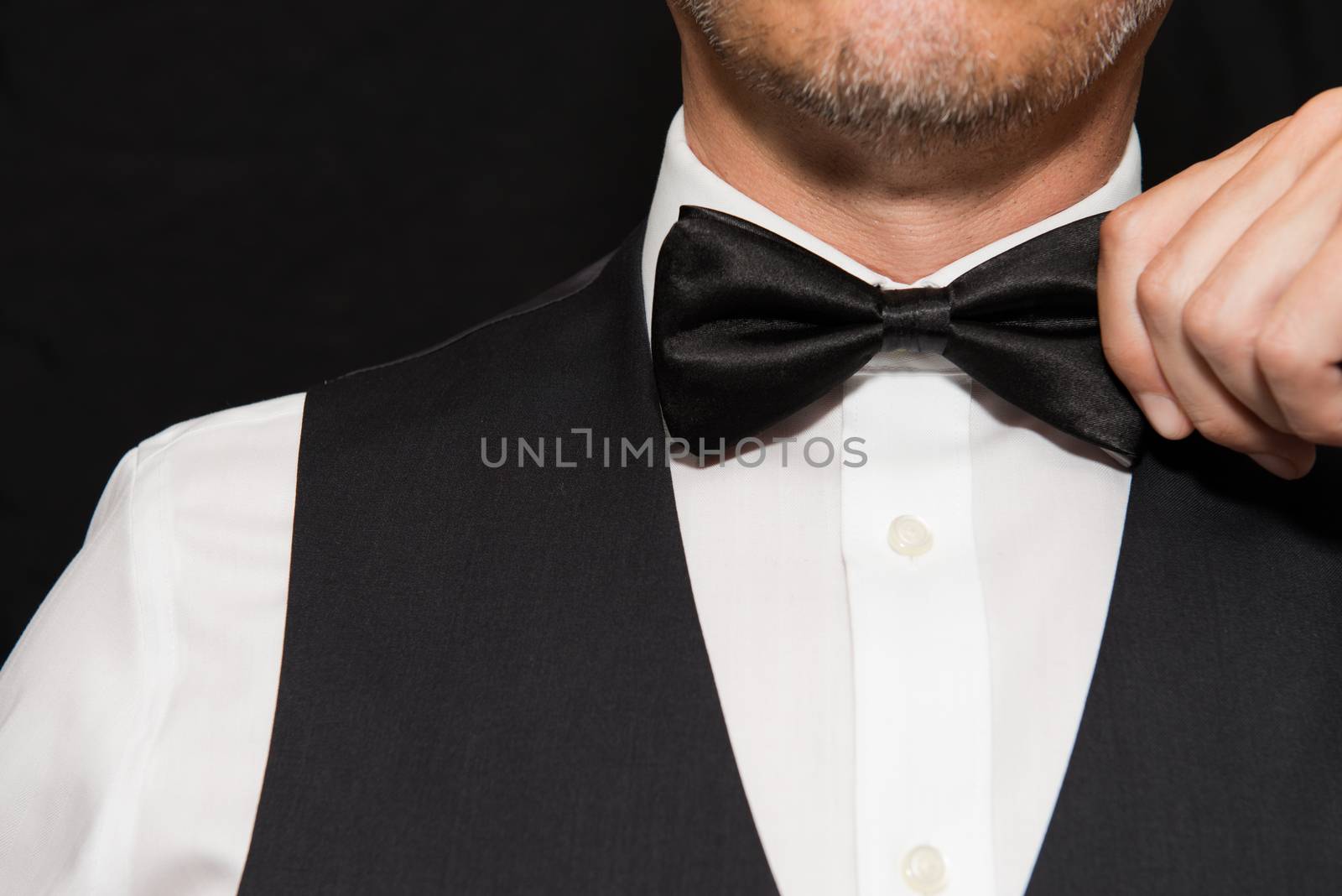 Close-up of a gentleman in a waistcoat straightening his bowtie.