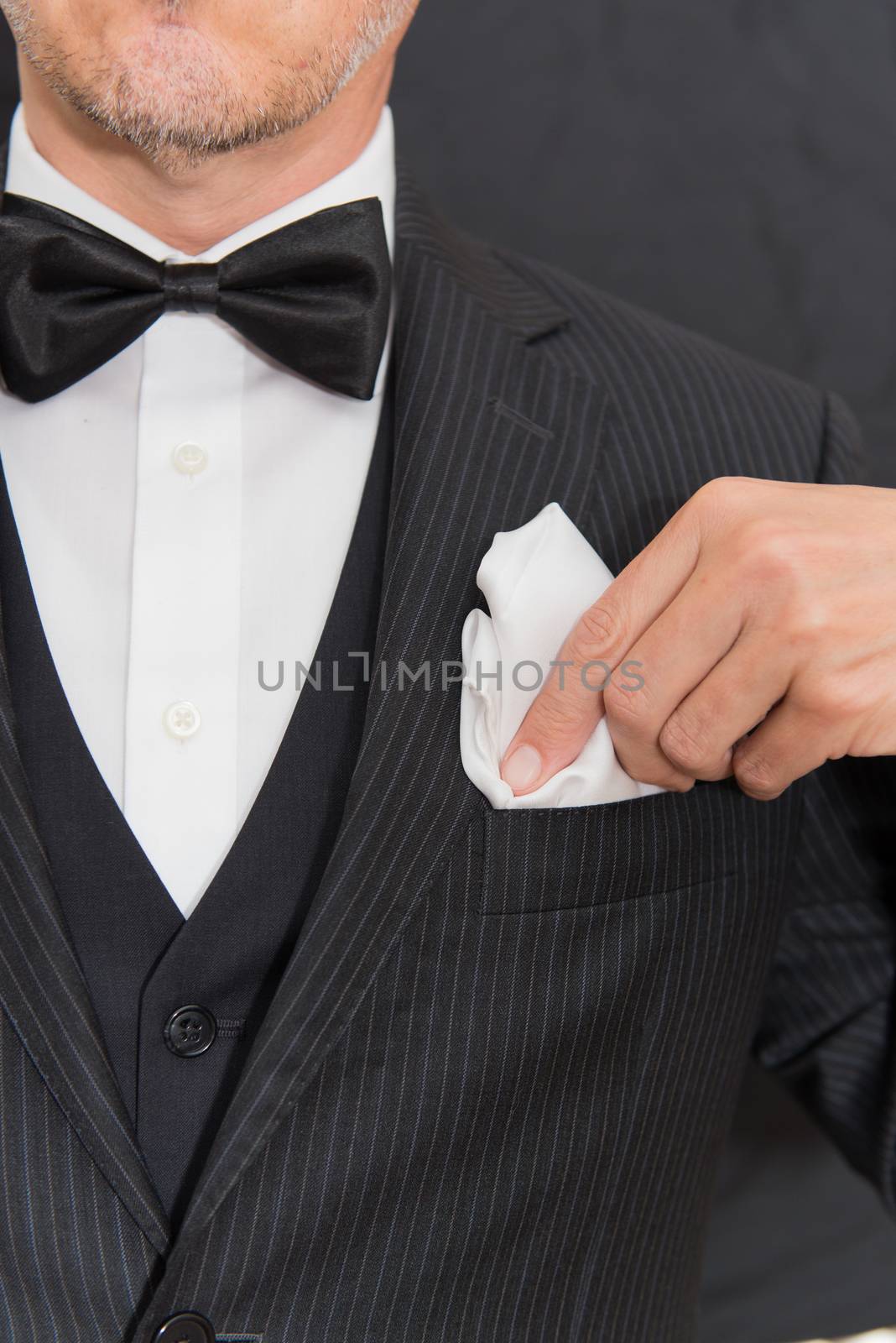 Close-up of a gentleman wearing Black Tie fixes his pocket square, vertical.