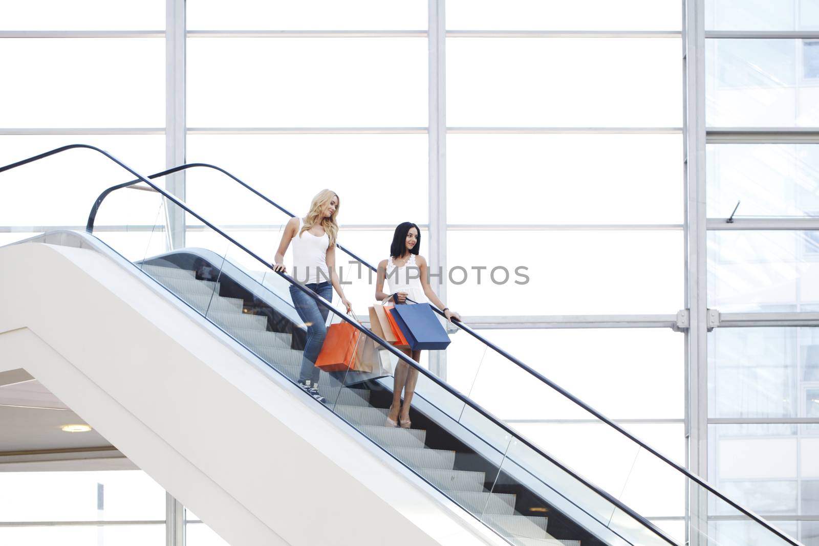 Young beautiful happy women on escalator of shopping mall