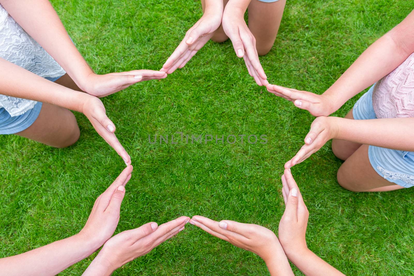 Arms of girls with hands making star shape above grass by BenSchonewille