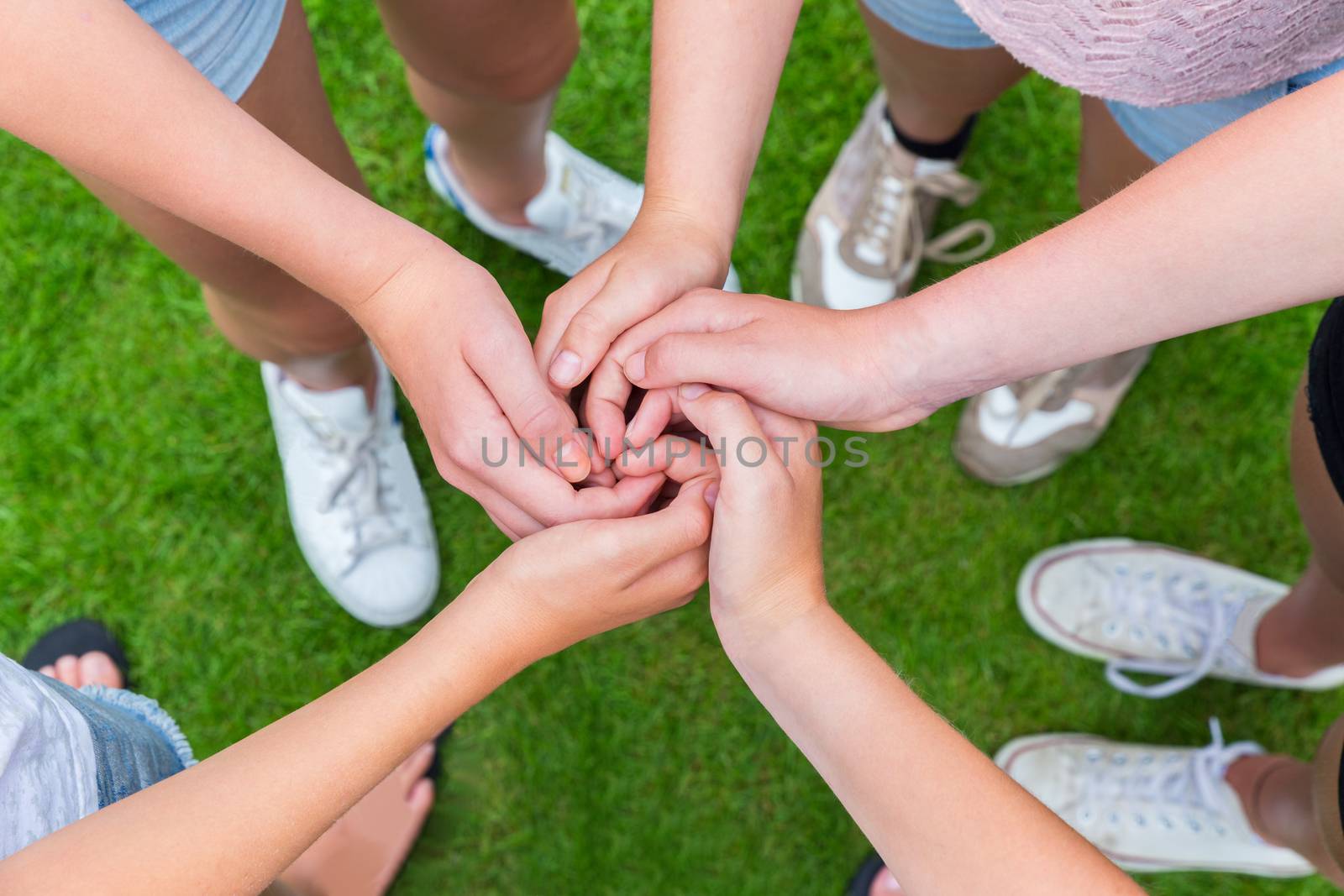 Five arms with hands of young girls entwined above green grass