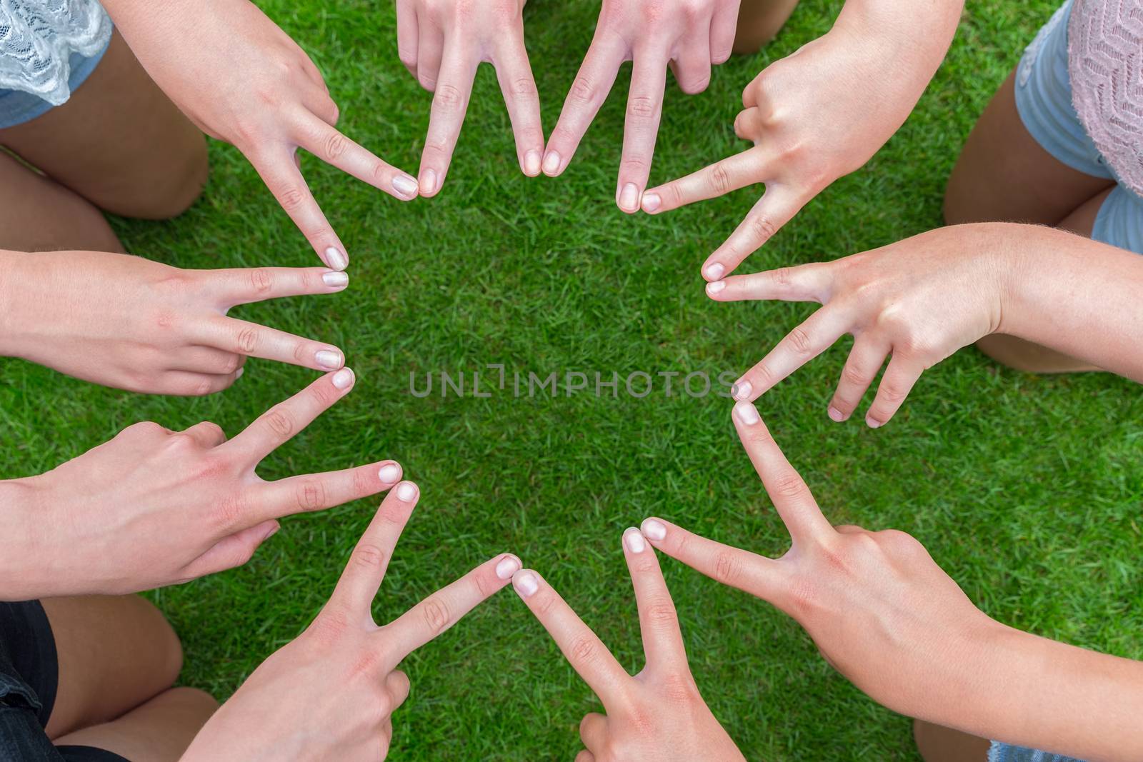 Many arms of girls with hands making ten pointed star above green grass