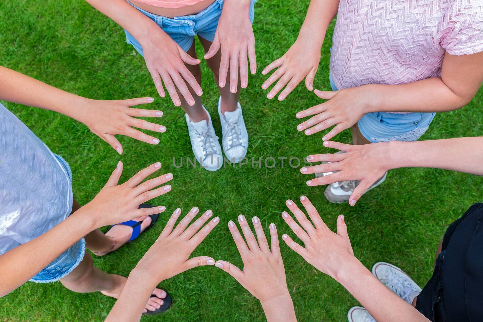 Many hands of young girls making circle above green grass