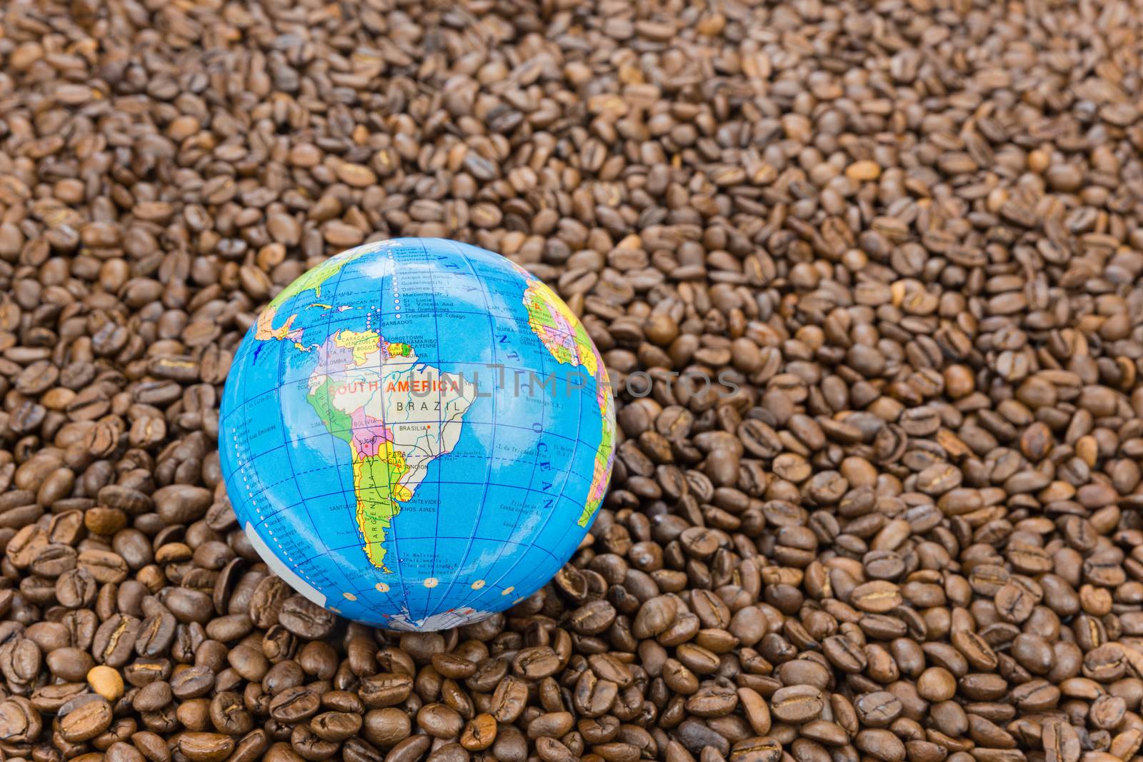 Many whole coffee beans with South America on little globe