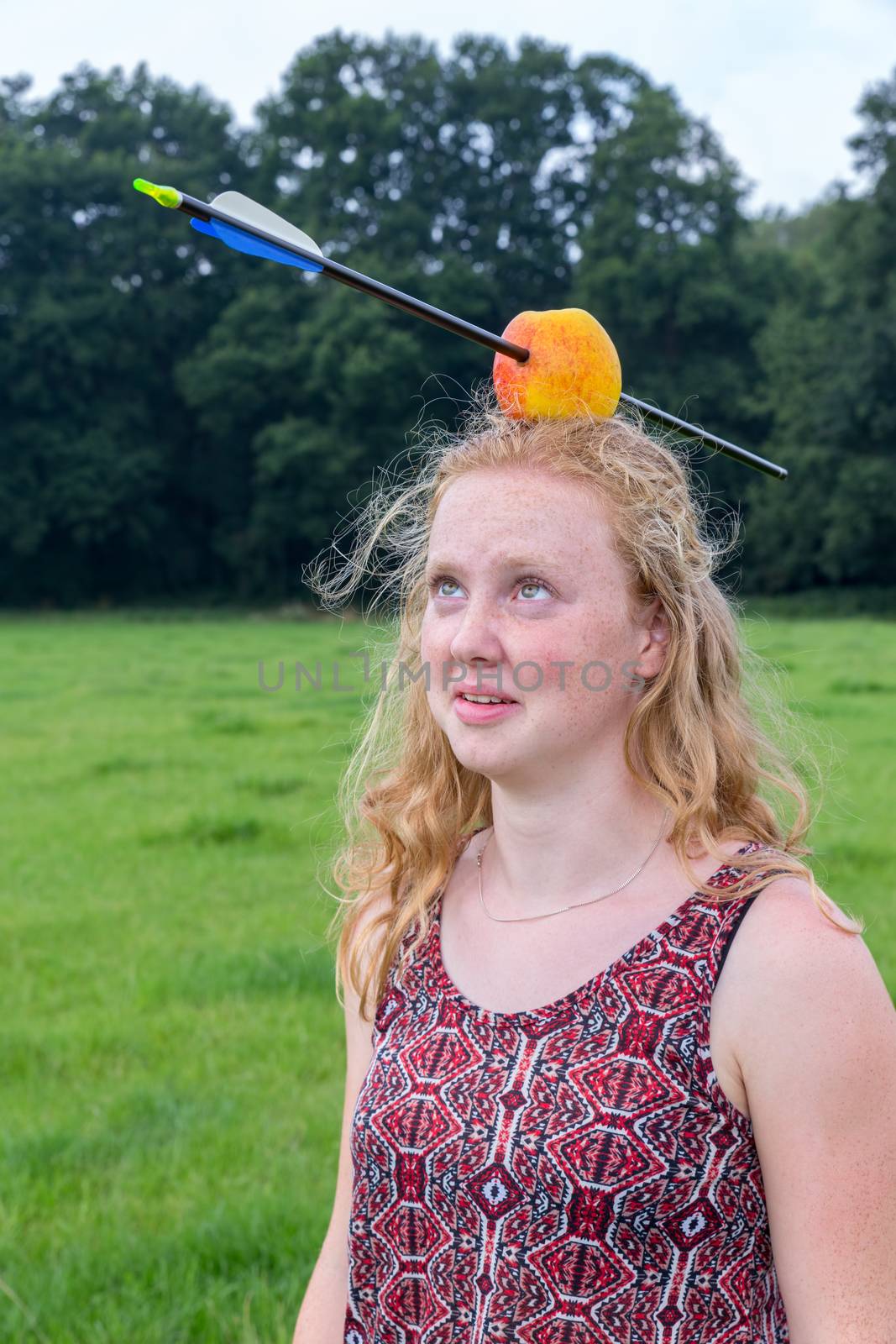 Young woman looking afraid at arrow in apple on head outdoors