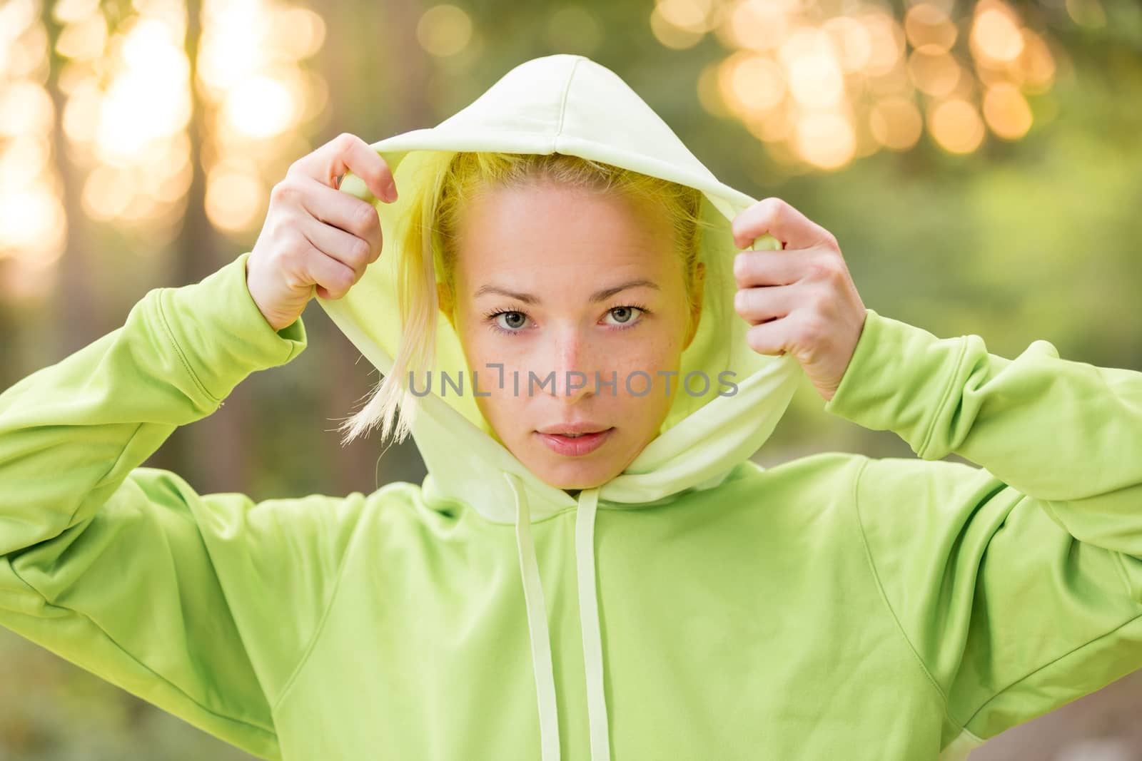 Portrait of attractive confident sporty woman wearing fashionable green hoodie while training in the nature. Active lifestyle and sportswear concept.