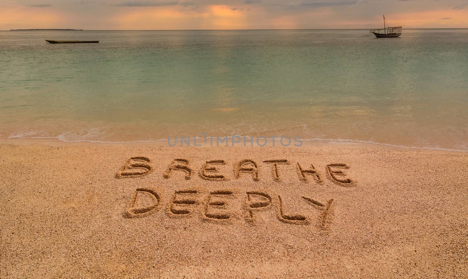 In the photo a beach in Zanzibar at sunset where there is an inscription on the sand "Breathe Deeeply".