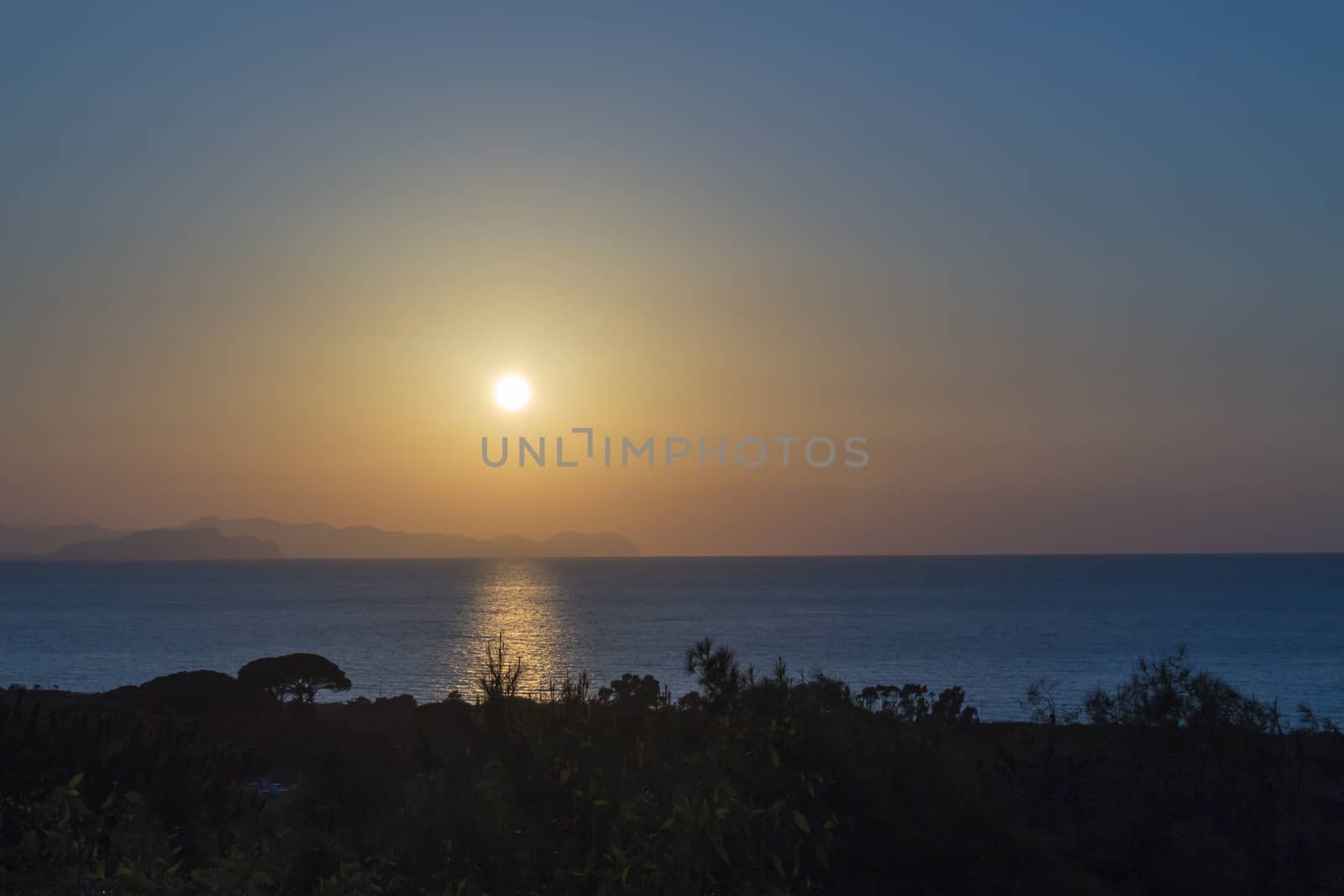 Sunset on the sea of sicily with trees.