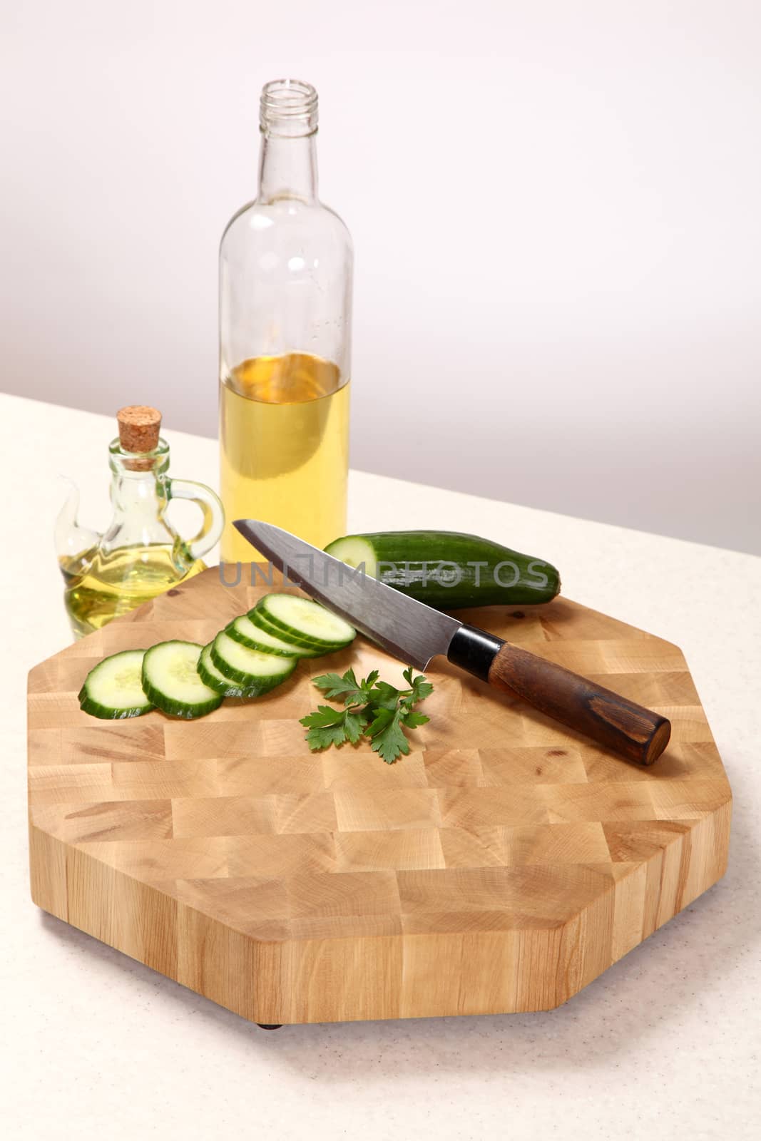 Cucumber knifed, a parsley leaf on a chopping board and sunflower oil in bottles