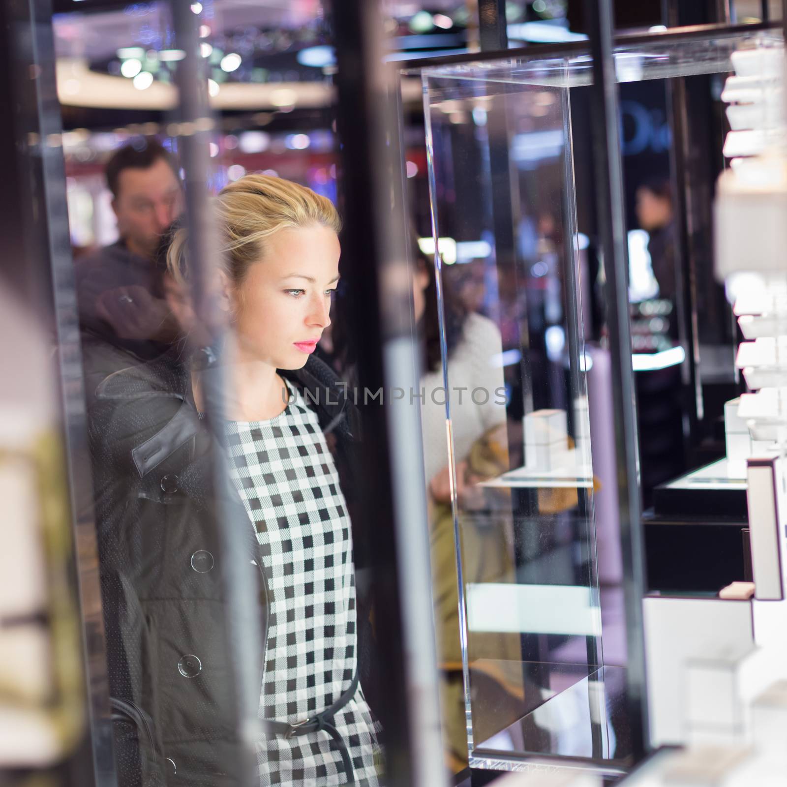 Beautiful blonde lady standing in front of showcase in beauty store, admiring new perfume collection.