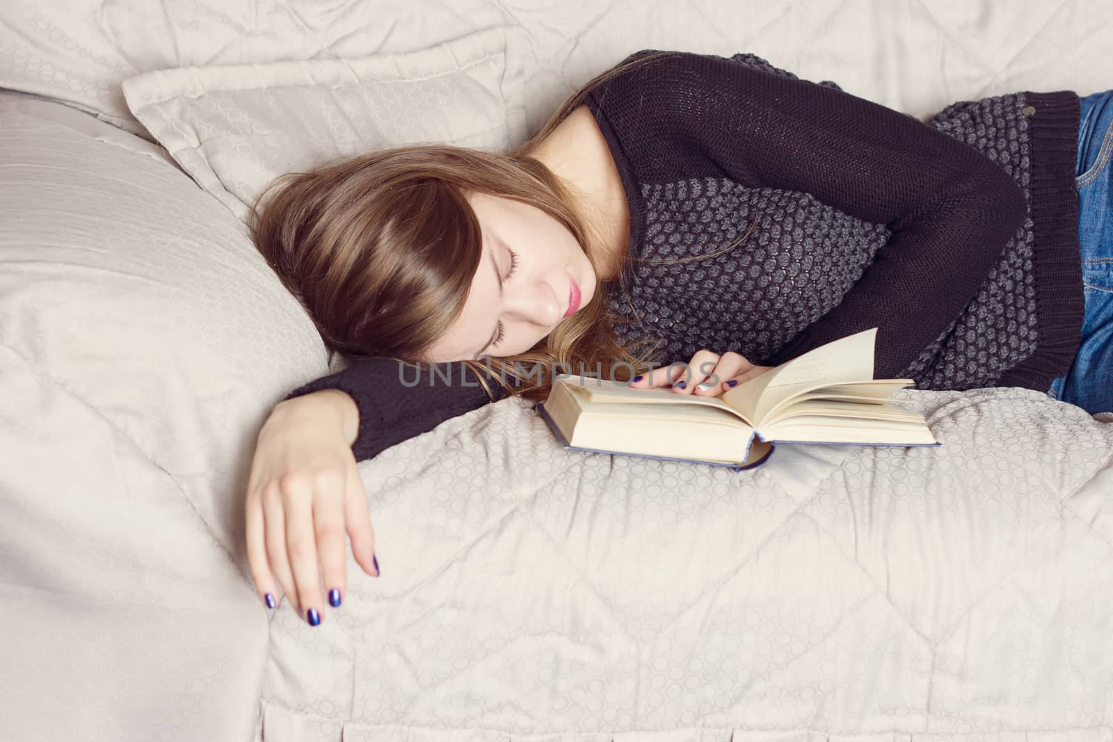 Attractive young female is sleeping on sofa at home with book.