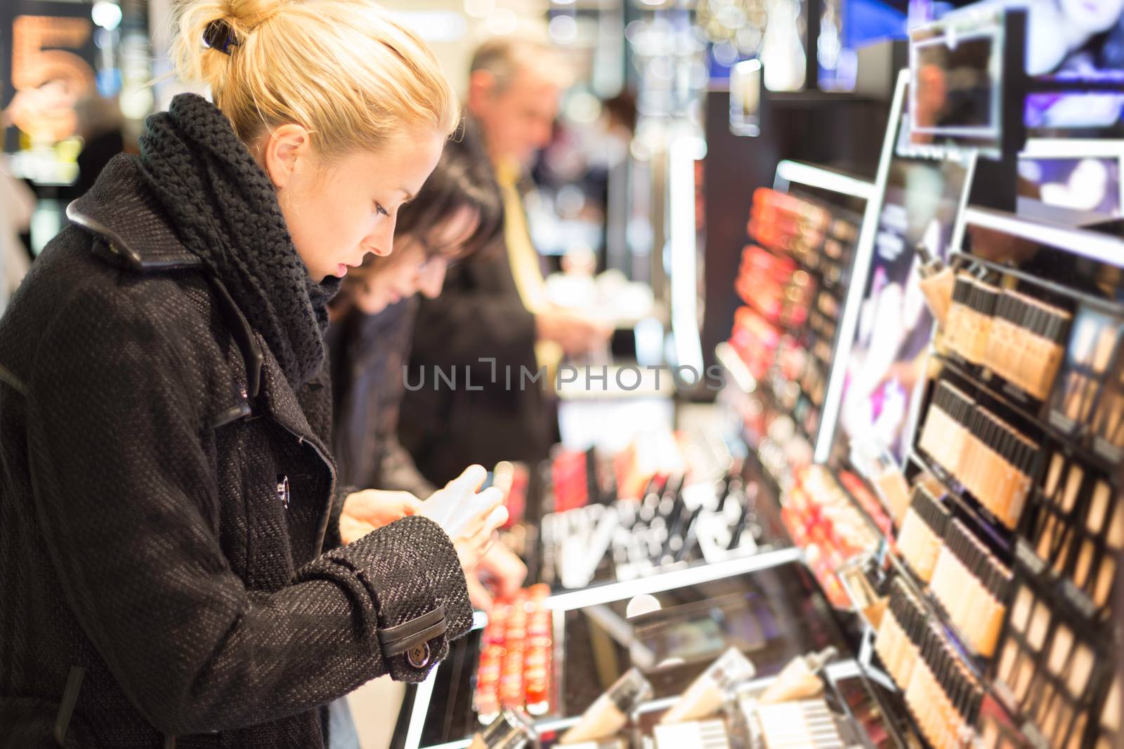 Beautiful blond lady testing  and buying cosmetics in a beauty store.