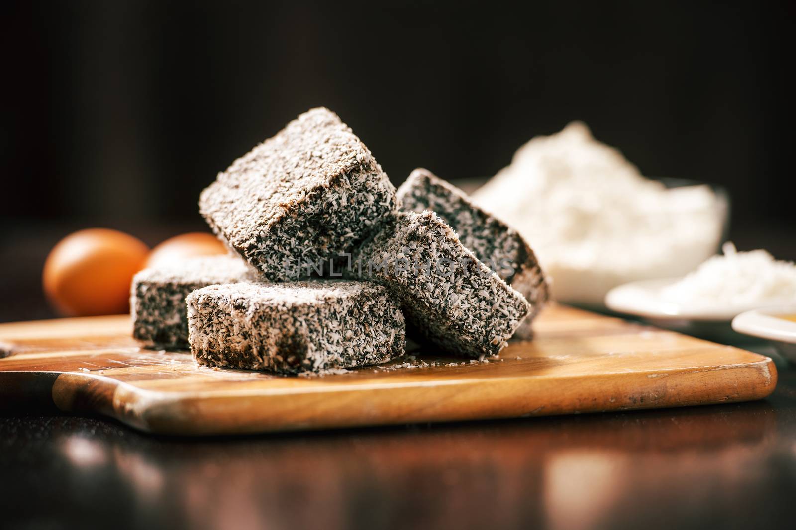 Group of Lamingtons on a timber cutting board with food ingredients in the background