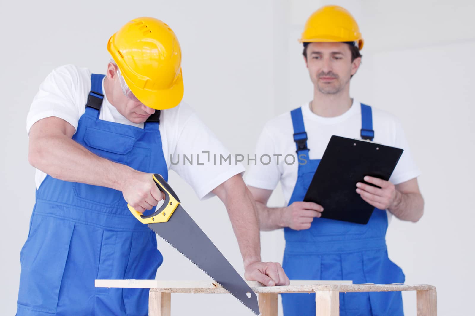 Two workmen in protective workwear with saw and folder