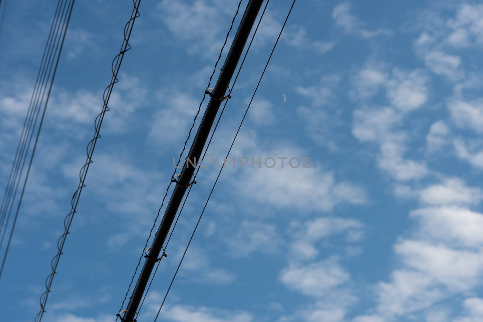 Black Power lines crossing a blue sky dappled with soft clouds and a cresent moon.