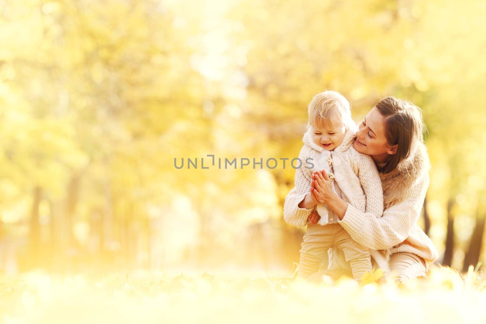 Mother and child having fun in autumn park among yellow leaves