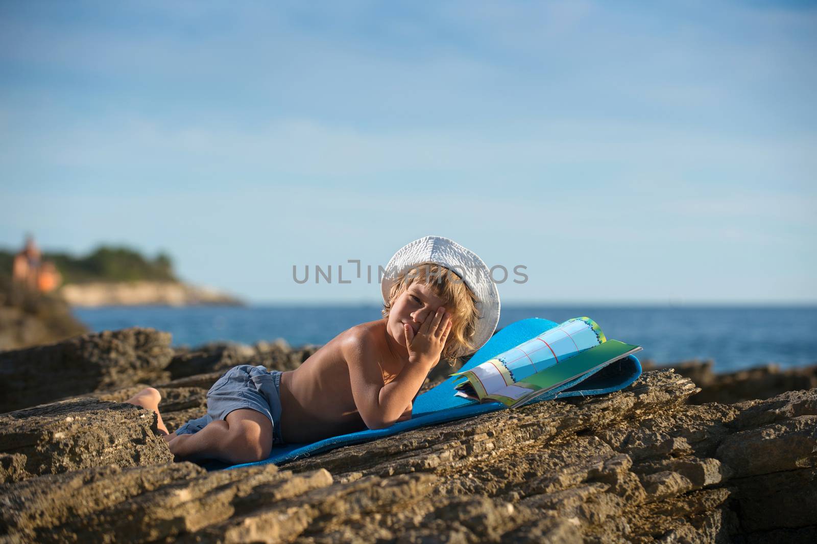 Little boy reading on the beach by kaliantye