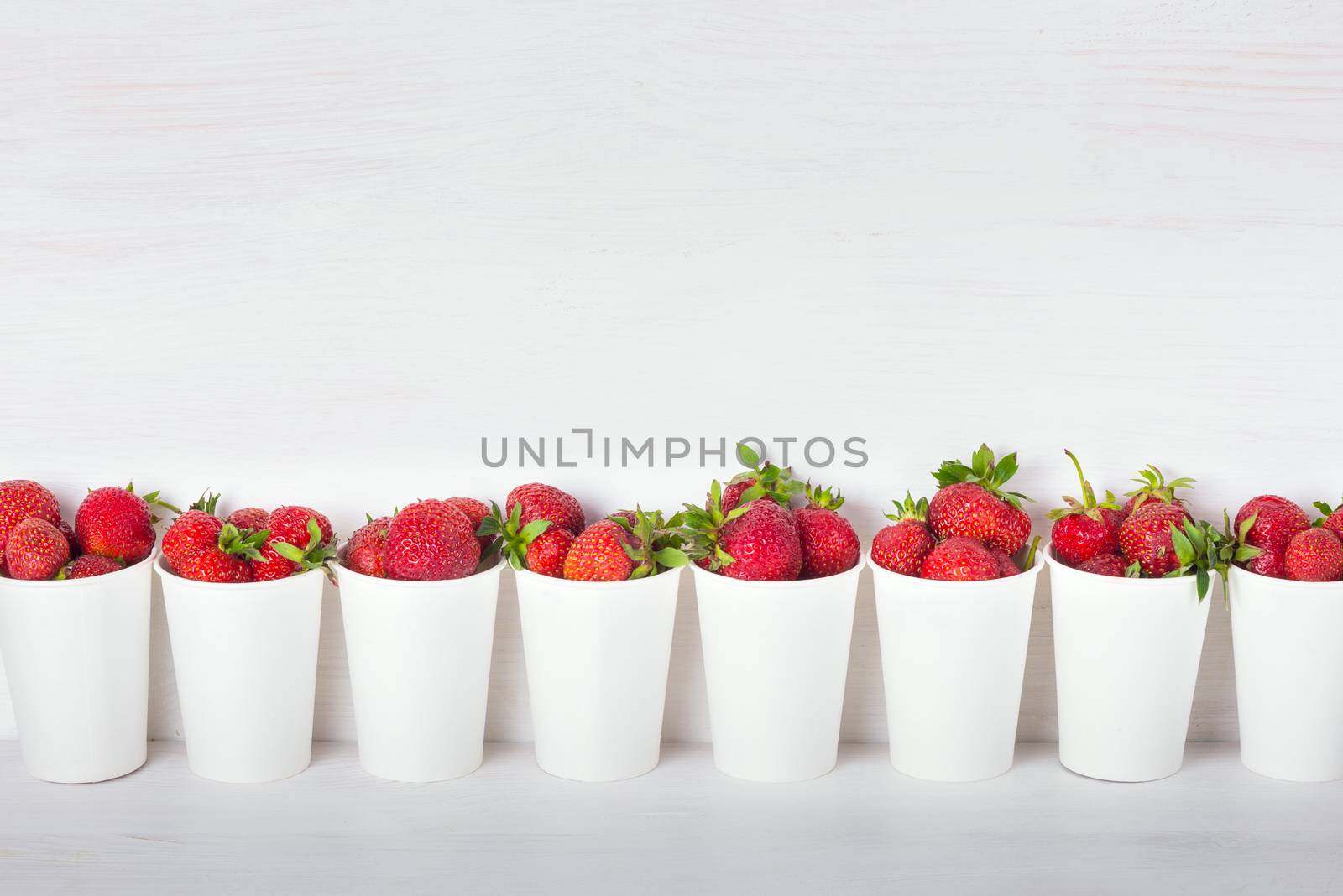 a series of white paper cups with fresh ripe delicious sweet strawberries on a white background