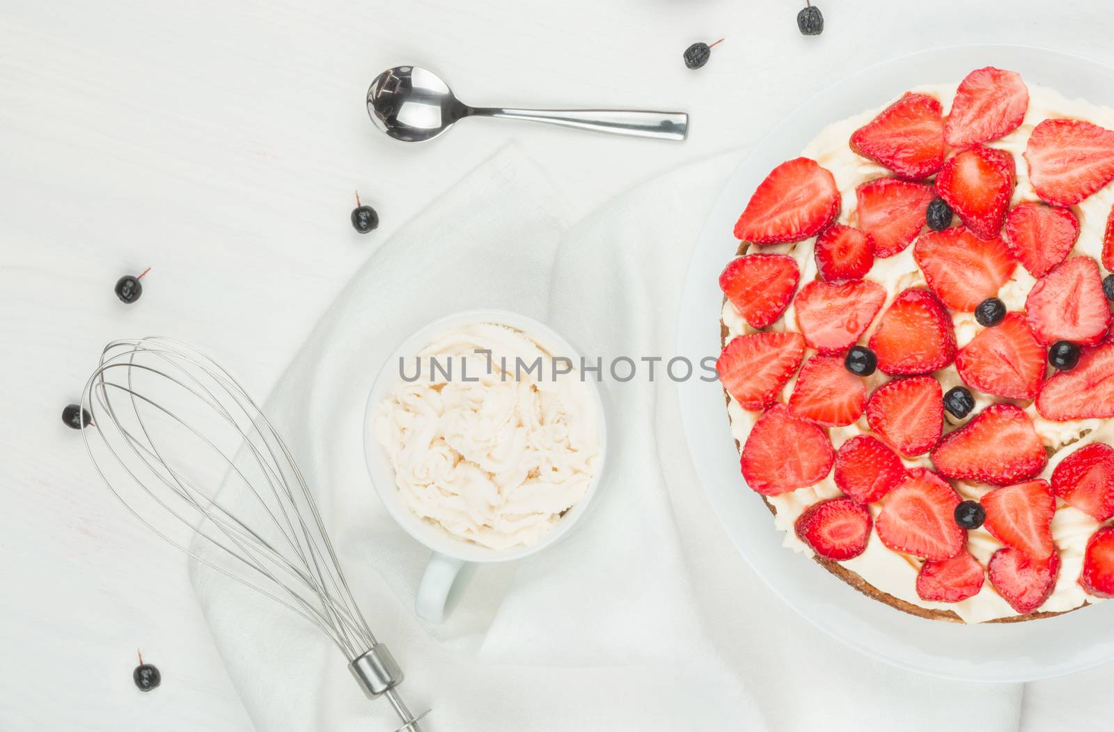 Delicious nutritious cake with fresh strawberries decorated with chokeberry, white cup with whipped cream, steel spoon, strawberry, napkin, knife,  plate, top view,  good morning