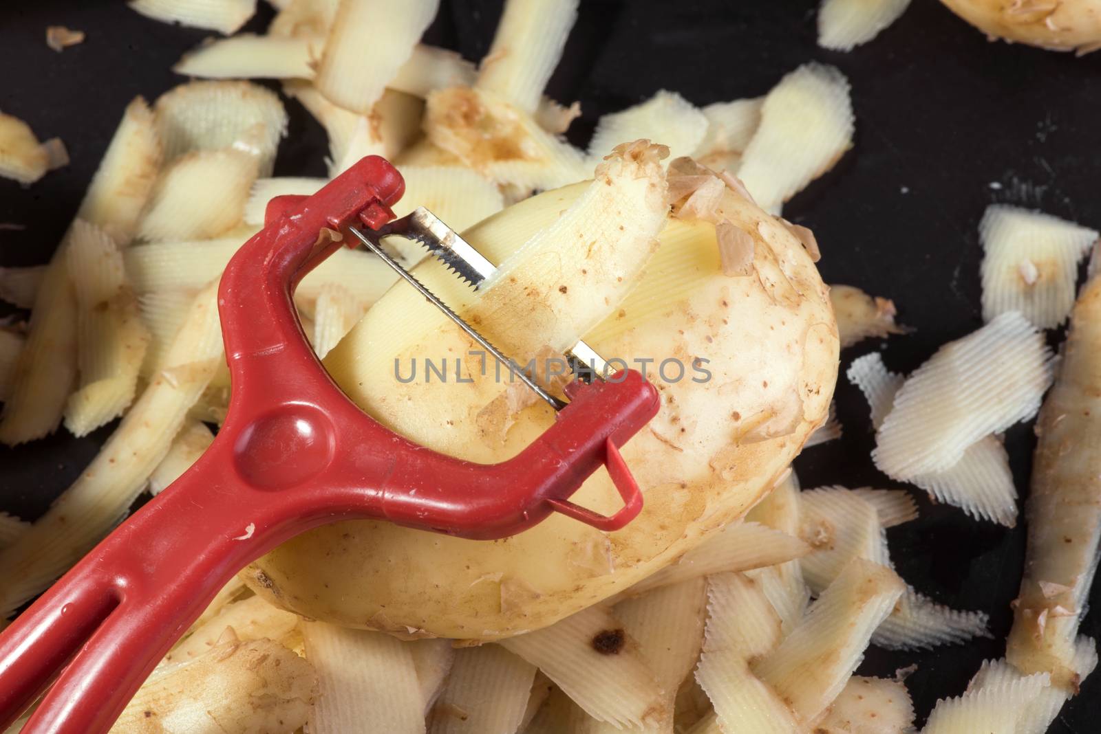 Vegetable peeler, raw potatoes and potato peels on black background, cooking potatoes