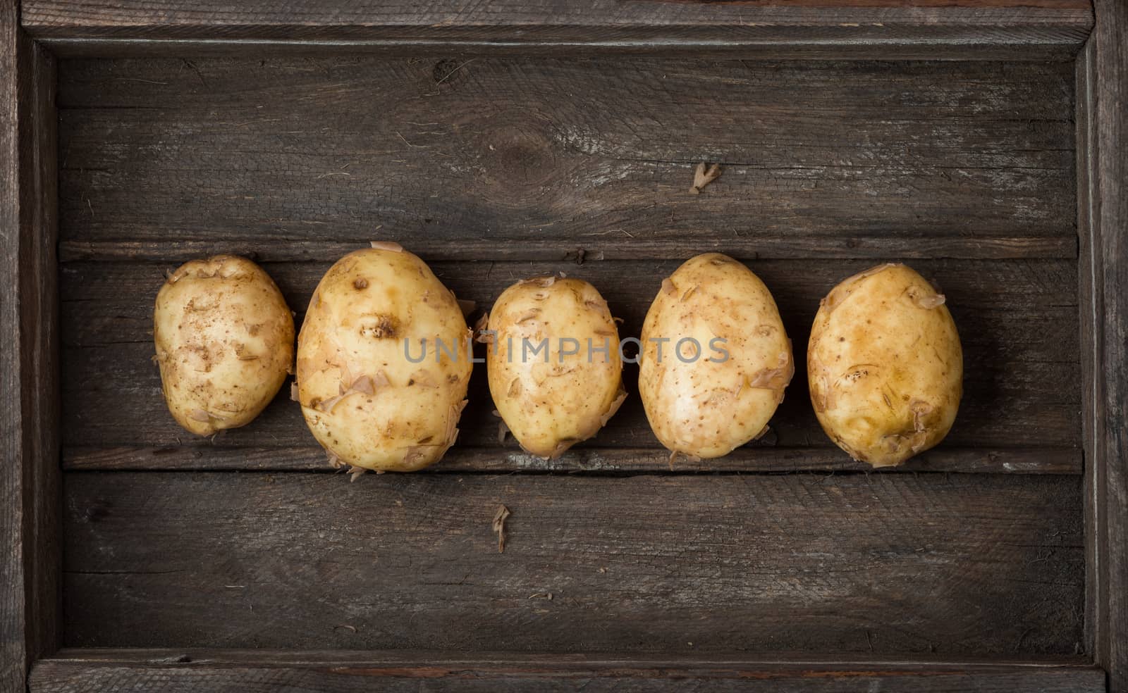 series of raw new potatoes in an old wooden box as background, top view. Harvest.