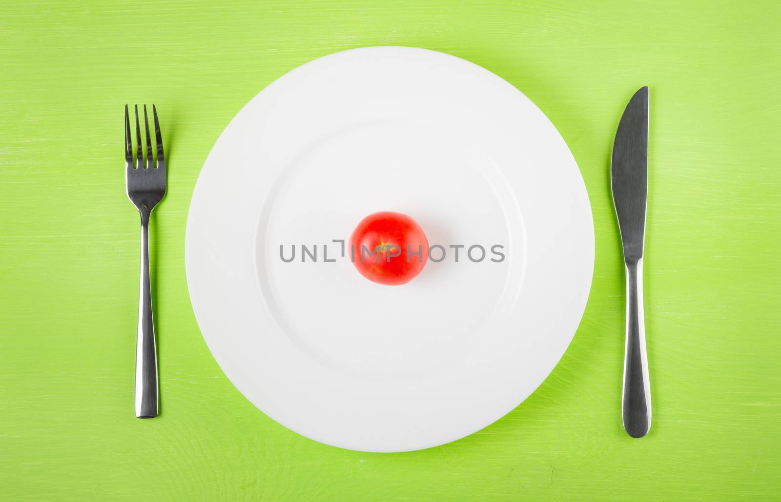 the concept of dietary restrictions, healthy lifestyle, diet,  weight loss, anti-obesity, healthy diet. Small tomato on a plate, knife, fork on the table, top view