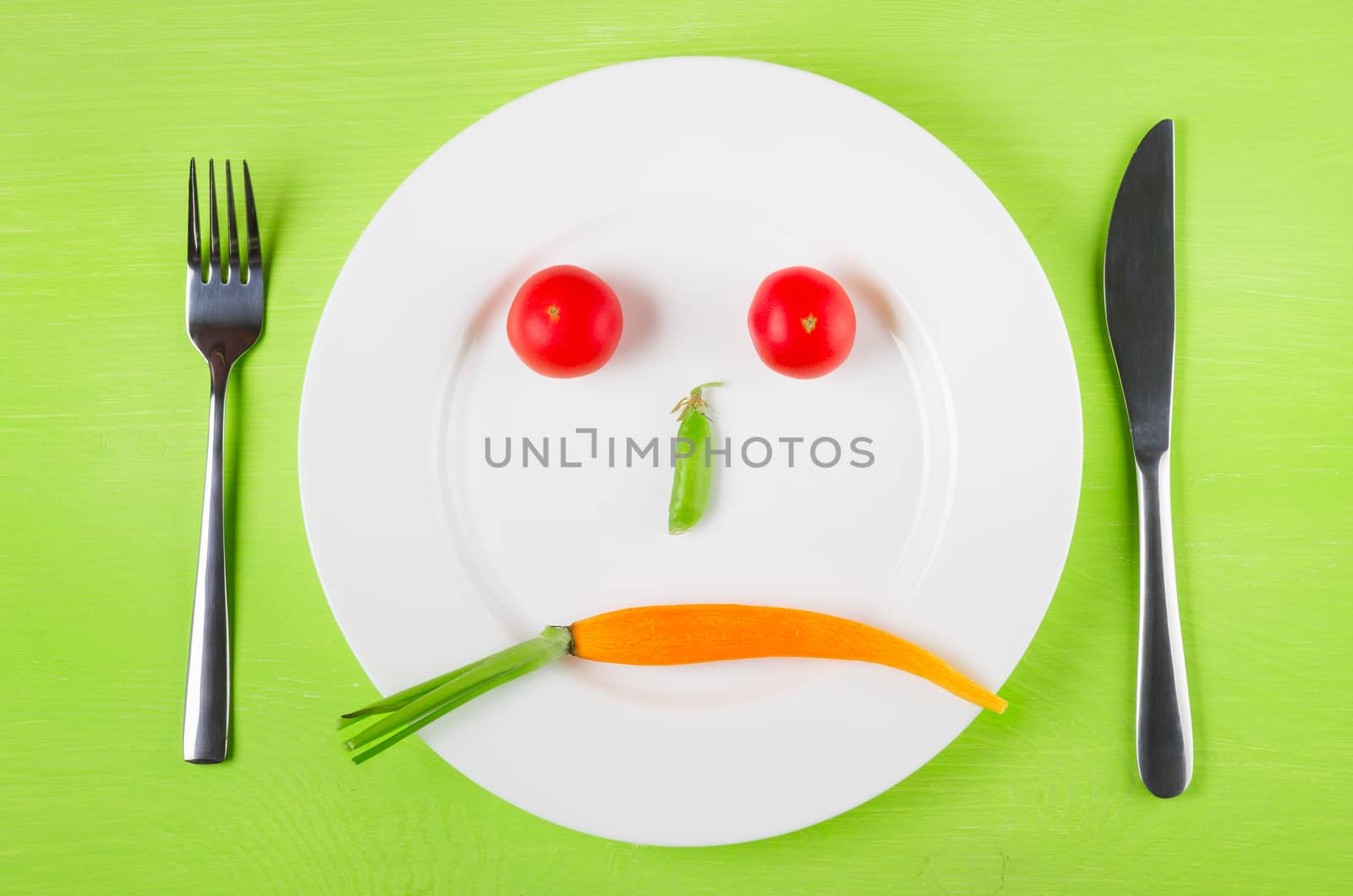 Sad face of vegetables, the concept of dietary restrictions, healthy lifestyle, diet,  weight loss, anti-obesity, healthy diet. Two tomatoes, peas in a pod and carrots on a plate, knife, fork