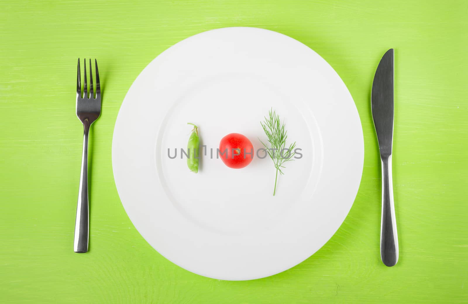 the concept of dietary restrictions, healthy lifestyle, diet,  weight loss, anti-obesity, healthy diet. Small tomato, green peas, a sprig of dill on a plate, knife, fork on the table, top view