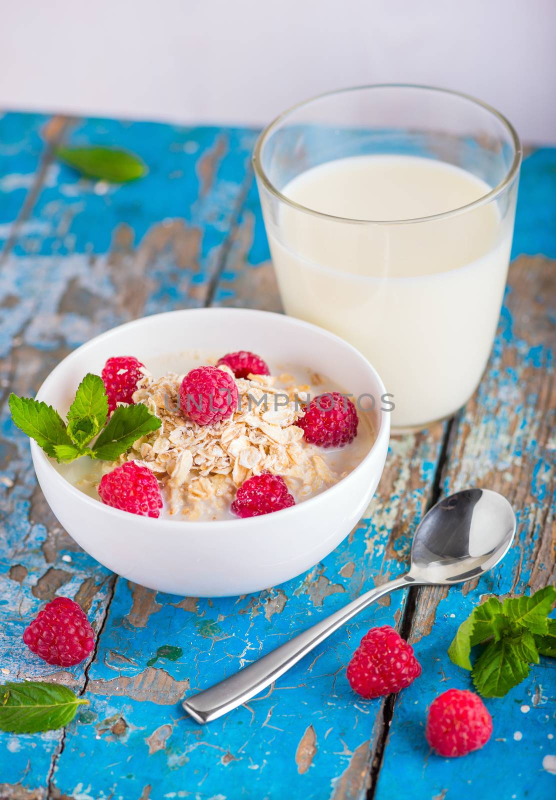 Oat flakes with milk and raspberries for breakfast, glass with milk, spoon,  fresh mint on an old wooden blue background, the concept of a healthy diet, weight loss