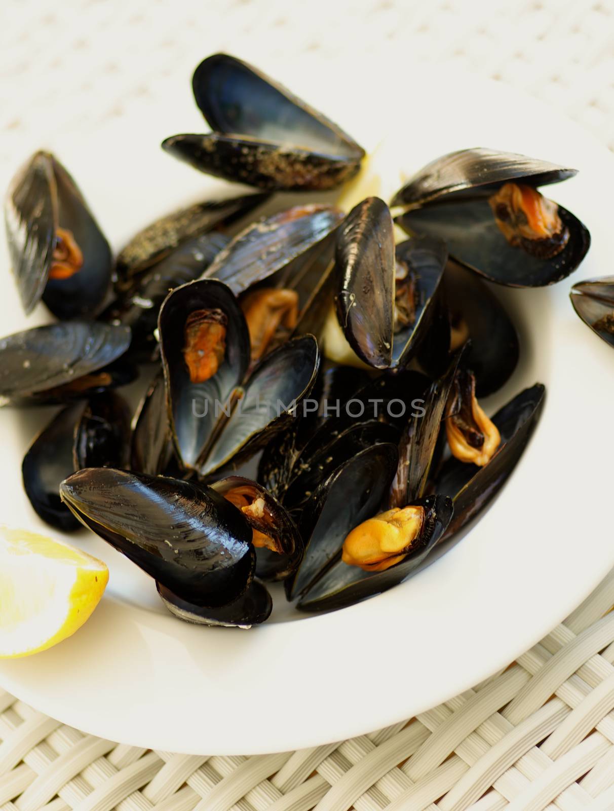 White Plate with Boiled Mussels and Lemon closeup on Wicker background