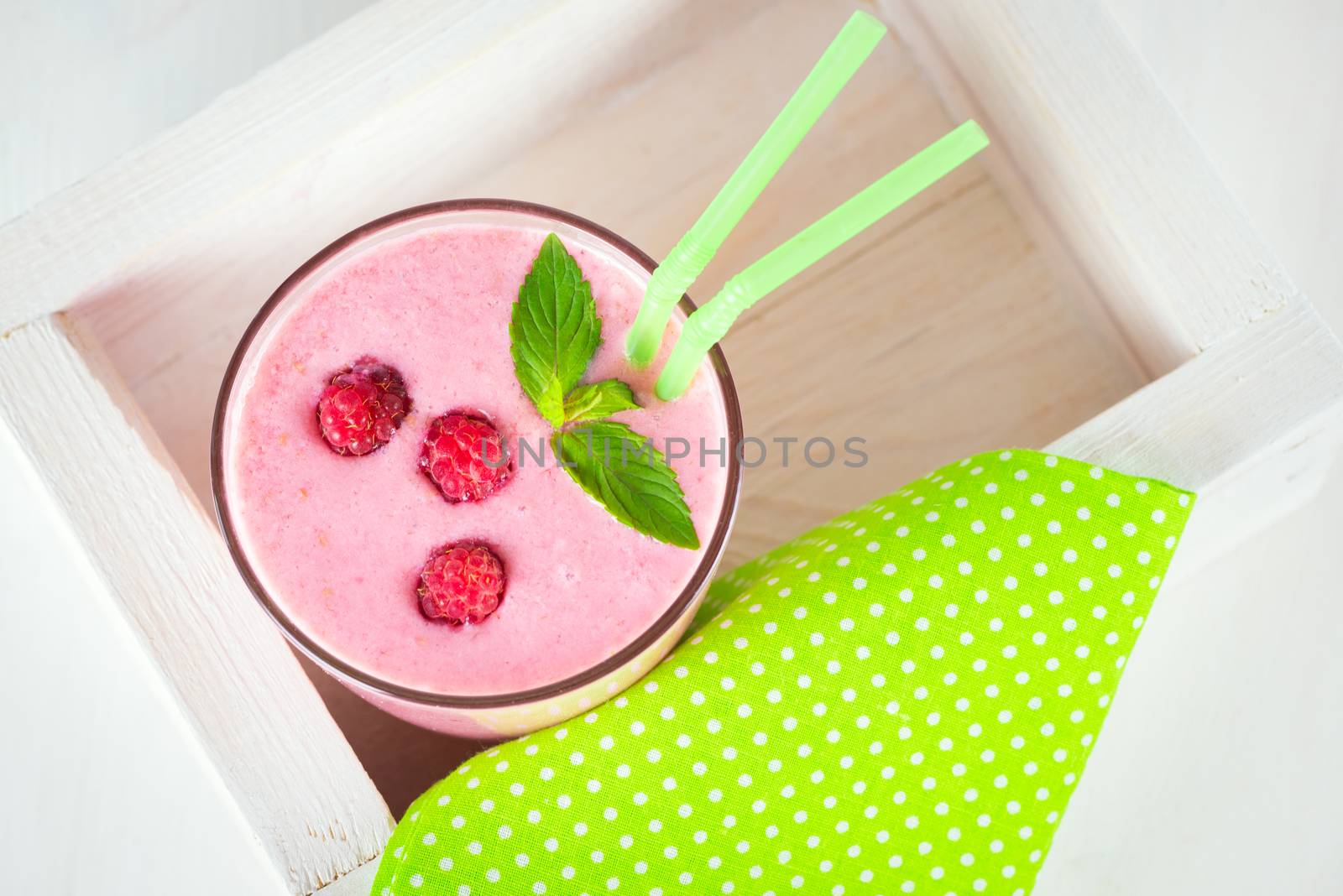 Raspberry dairy smoothie with fresh berries and sprig of mint with two green cocktail stick in a decorative box on a white wooden table