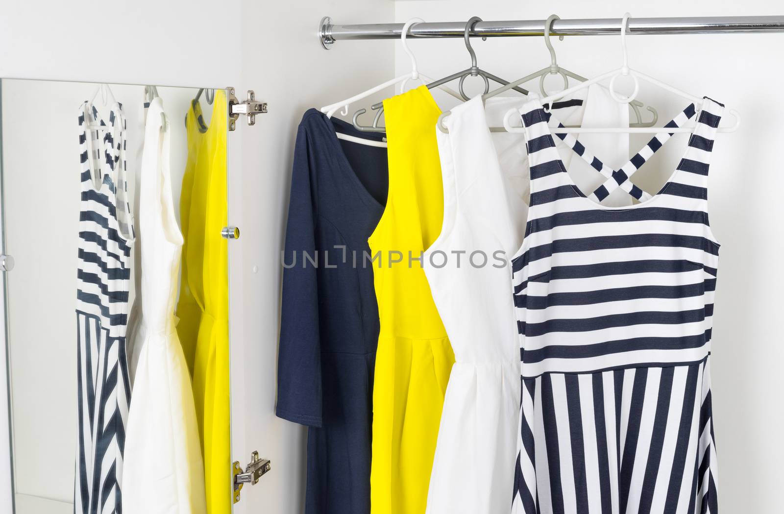 a series of bright modern fashion women's dresses on hangers in a white cupboard for summer and spring