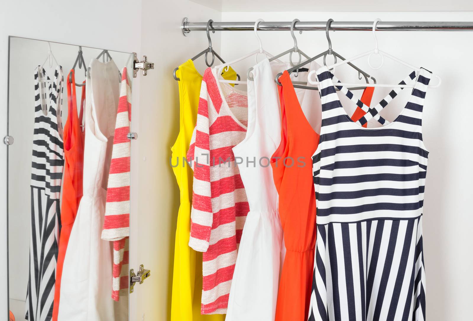 a series of bright modern fashion women's dresses on hangers in a white cupboard for summer and spring